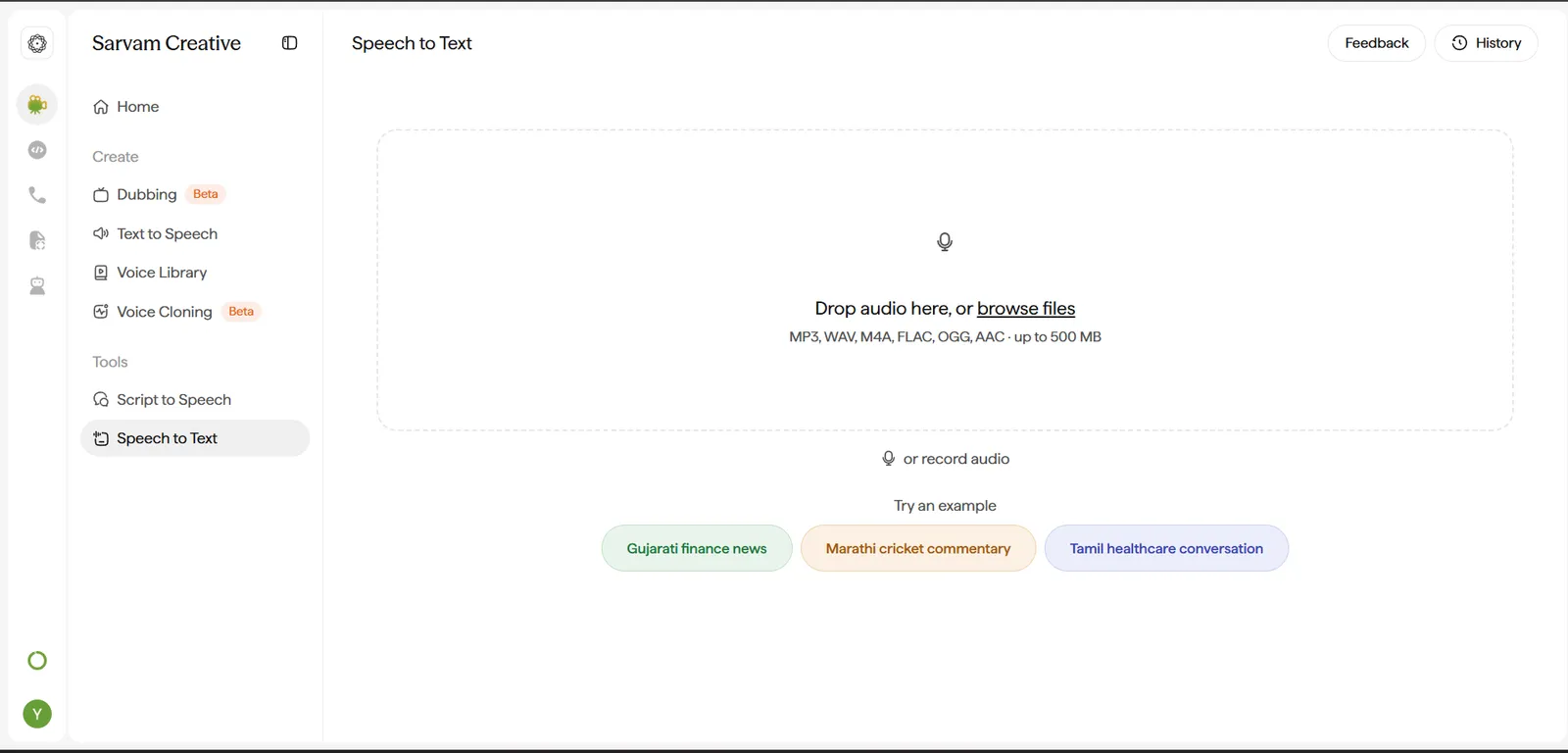 Speech to Text screen. Header has Feedback and History buttons. The main panel is a dashed-border drop zone with a microphone icon reading Drop audio here, or browse files, with the caption listing supported formats and a 500 MB size limit. Below it, a second option reads or record audio with its own microphone icon. Below that, Try an example offers three colored example chips: Gujarati finance news, Marathi cricket commentary, and Tamil healthcare conversation.