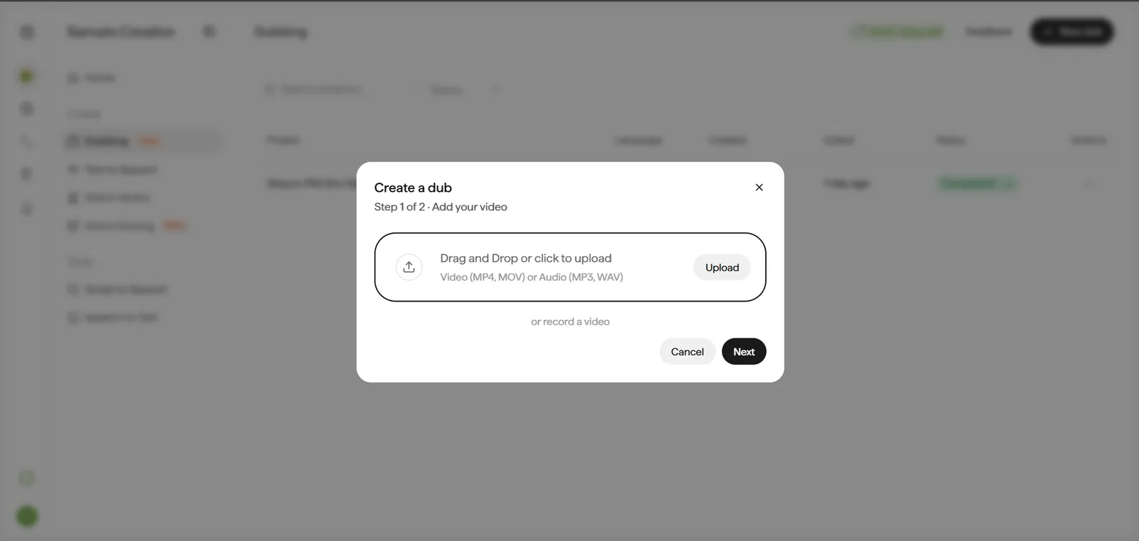 Create a dub modal, Step 1 of 2, titled Add your video, shown over a blurred background list of past dub projects. A bordered dropzone reads Drag and Drop or click to upload, with the caption Video (MP4, MOV) or Audio (MP3, WAV) and an Upload button on the right. Below the dropzone, a text link reads or record a video. The modal footer has Cancel and Next buttons.